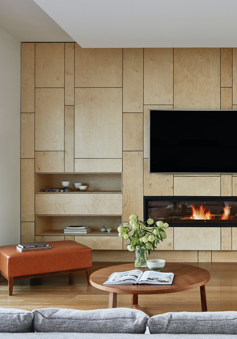 Zu sehen ist eine moderne TV Wohnwand vom Schreiner nach Maß mit integrierten Fächern und einem Kamin. Ebenso ein runder moderner Couchtisch aus Holz.